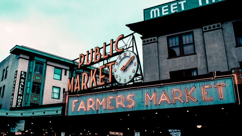 The image shows a neon-lit sign for a "Public Market" and "Farmers Market" in an urban area, likely a well-known market or landmark.